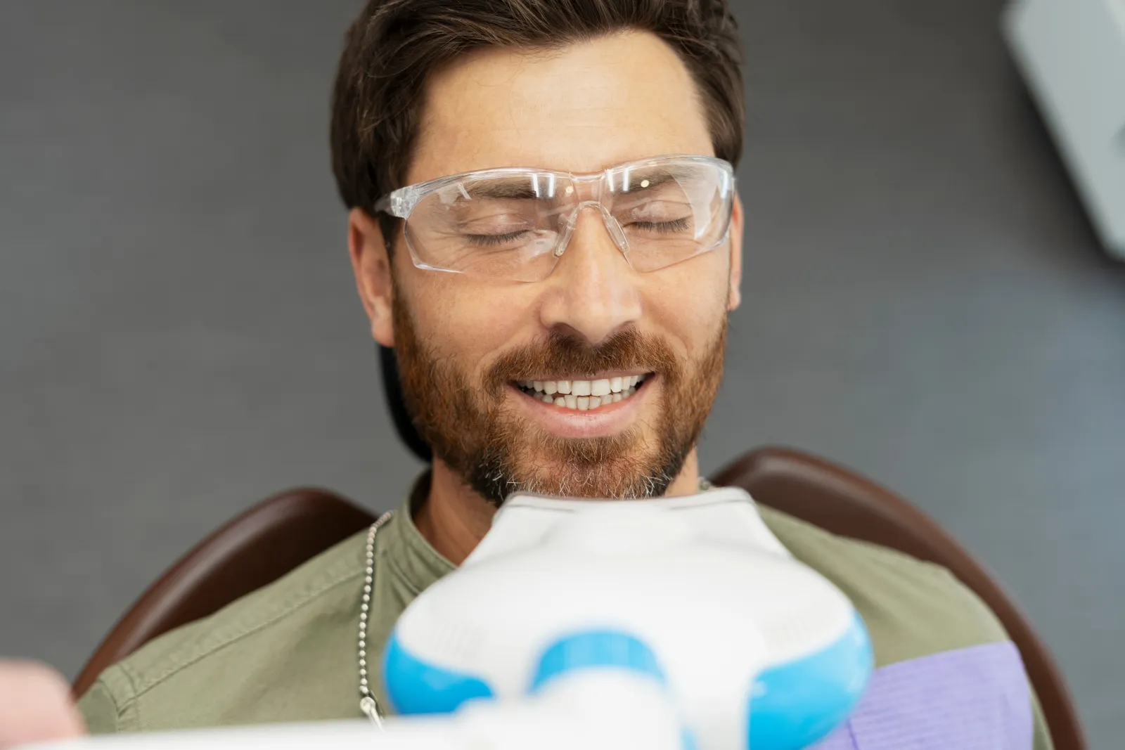 Portrait of handsome bearded man sitting in dental chair, wearing glasses with closed eyes