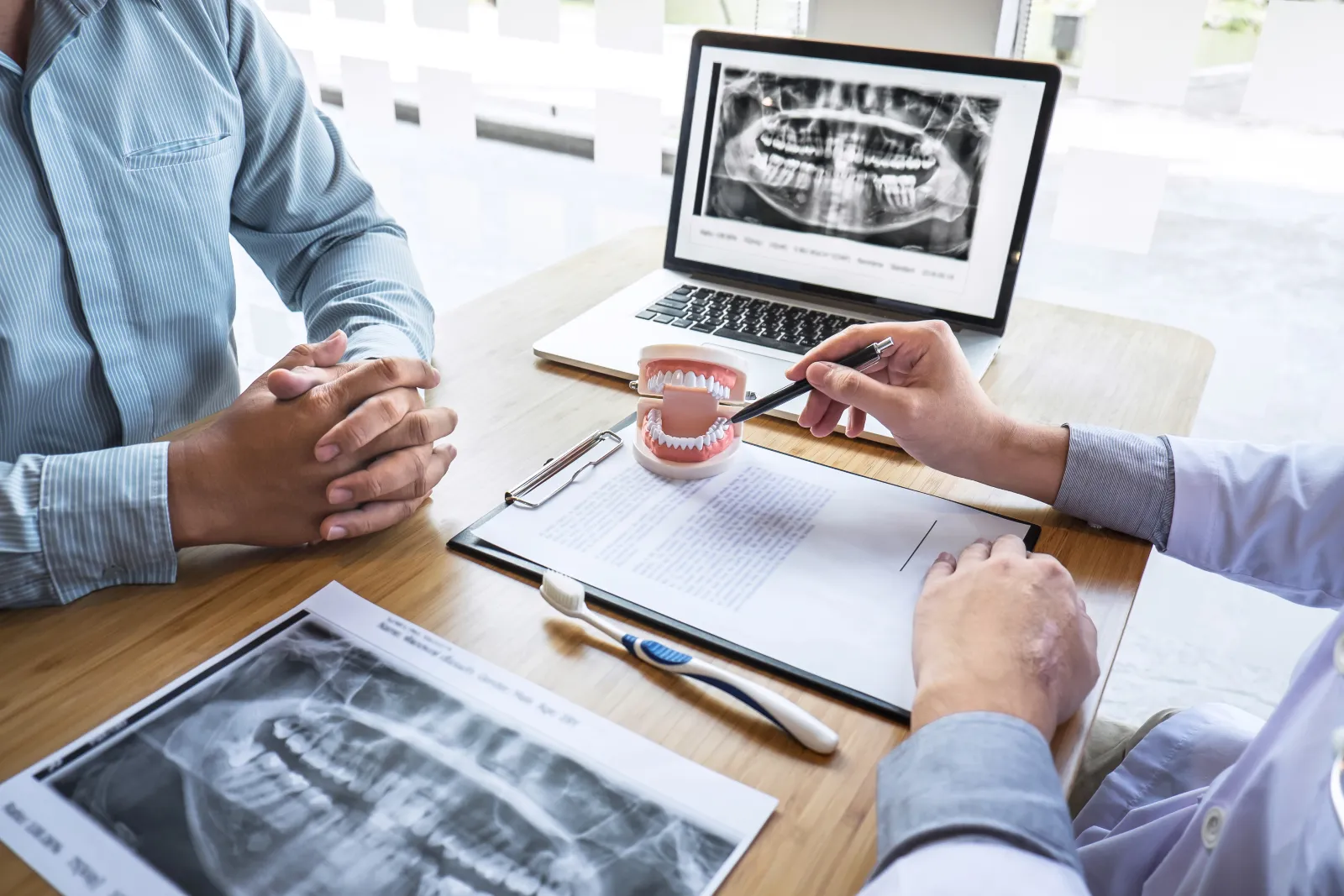 Professional Dentist showing jaw and teeth the x-ray photograph and discussing during explaining the consultation treatment issues with patient and writing history list on report